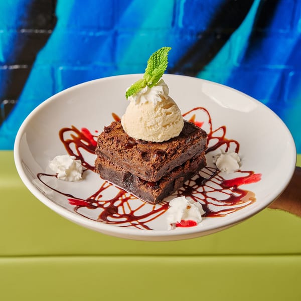 Two stacked brownies topped with vanilla ice cream, mint, whipped cream, and chocolate and raspberry drizzle.