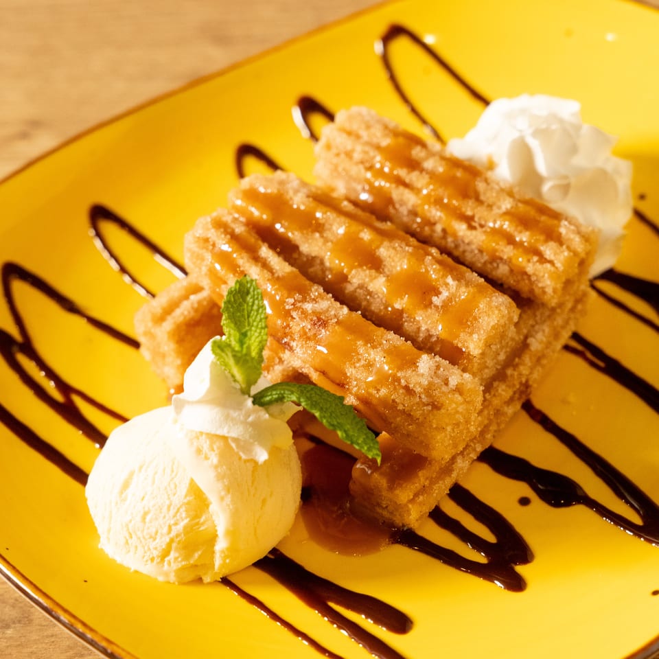 Churros drizzled with caramel sauce, served with vanilla ice cream and whipped cream on a yellow plate.