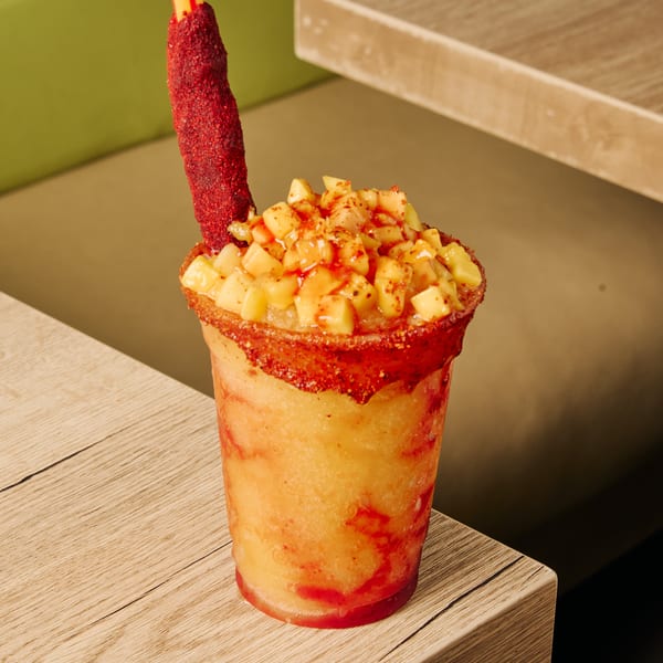 A vibrant mango chamoyada with diced mango, chili powder rim, and a tamarind candy straw.