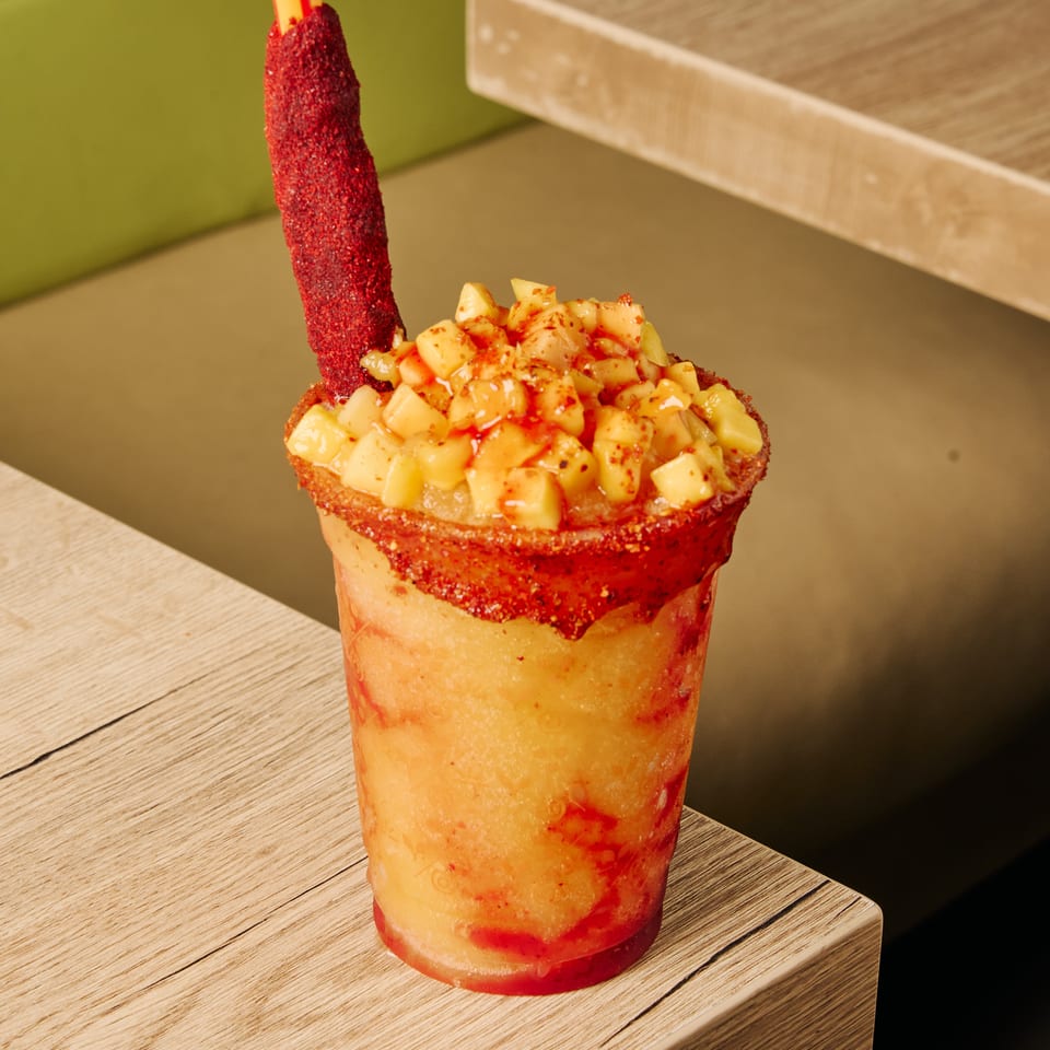 A vibrant mango chamoyada with diced mango, chili powder rim, and a tamarind candy straw.
